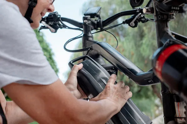 Mujer ciclista colocando la batería en el cuadro de una bicicleta eléctrica equipada con lo qué es un gestor de carga inteligente.