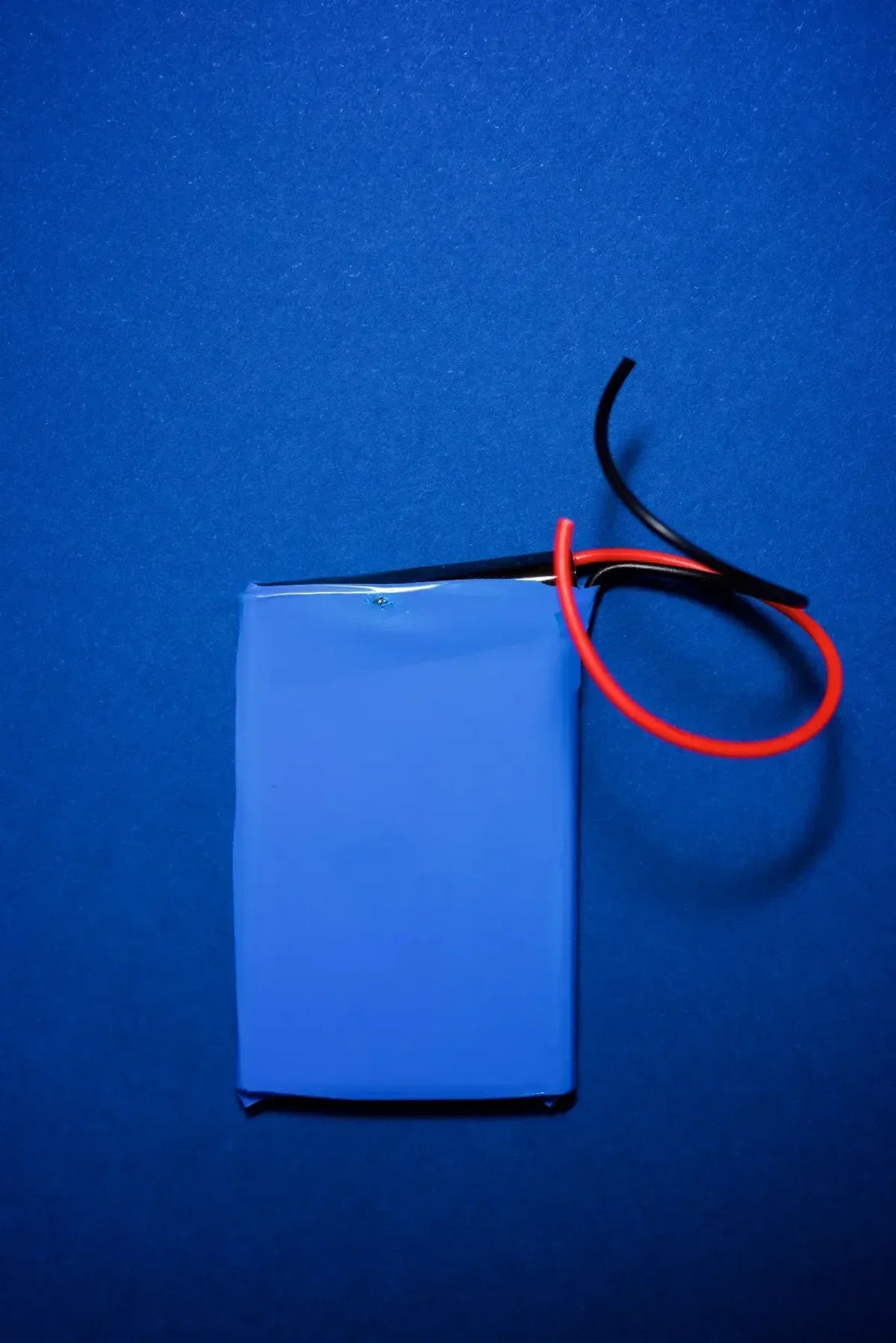 Primer plano de una pila de litio rectangular azul. Tiene cables rojo y negro listos para ser conectados.