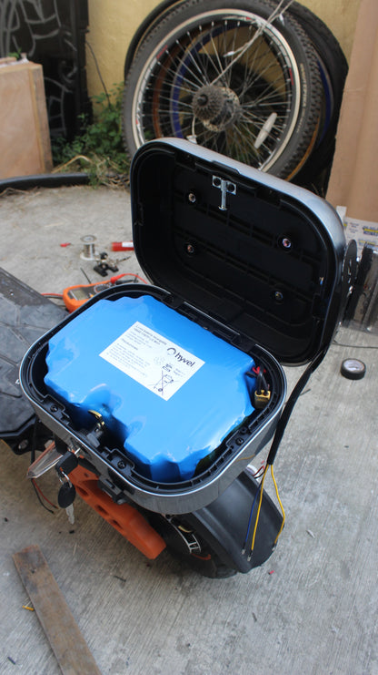 Imagen de la Batería compatible con cajuela de Honey Whale H3 siendo colocada en una moto eléctrica con una llanta de fondo. 